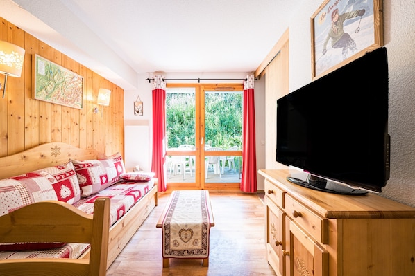 A wooden room with a sofa, a television, and a view through a glass door. - Quiet Apartment at the Foot of the Slopes (Valmeinier)