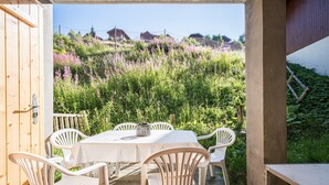 An outdoor patio with a table and chairs, surrounded by a wooden deck and a view of a hillside with vegetation. - Quiet Apartment at the Foot of the Slopes (Valmeinier)