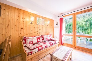 A wooden-paneled room with a bed, a bench, and a view of greenery outside. - Quiet Apartment at the Foot of the Slopes (Valmeinier)