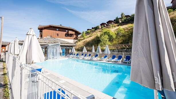 A swimming pool with lounge chairs and umbrellas, surrounded by a white fence. - Quiet Apartment at the Foot of the Slopes (Valmeinier)