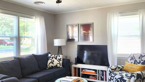 A living room with a sofa, armchair, coffee table, TV, and bookshelf. - SPOTLESS Geneva home!  MINUTES to Wineries, Spires, Downtown, & the Strip! (Geneva)