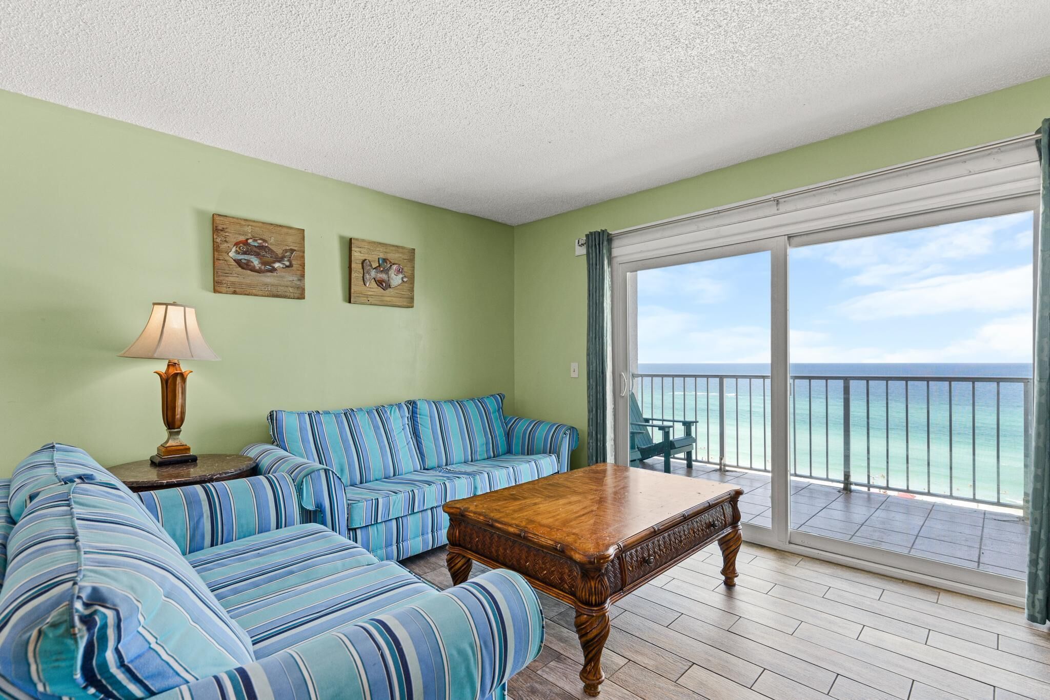 A room with a striped sofa, a wooden coffee table, a lamp, and a view of the ocean through a sliding glass door.