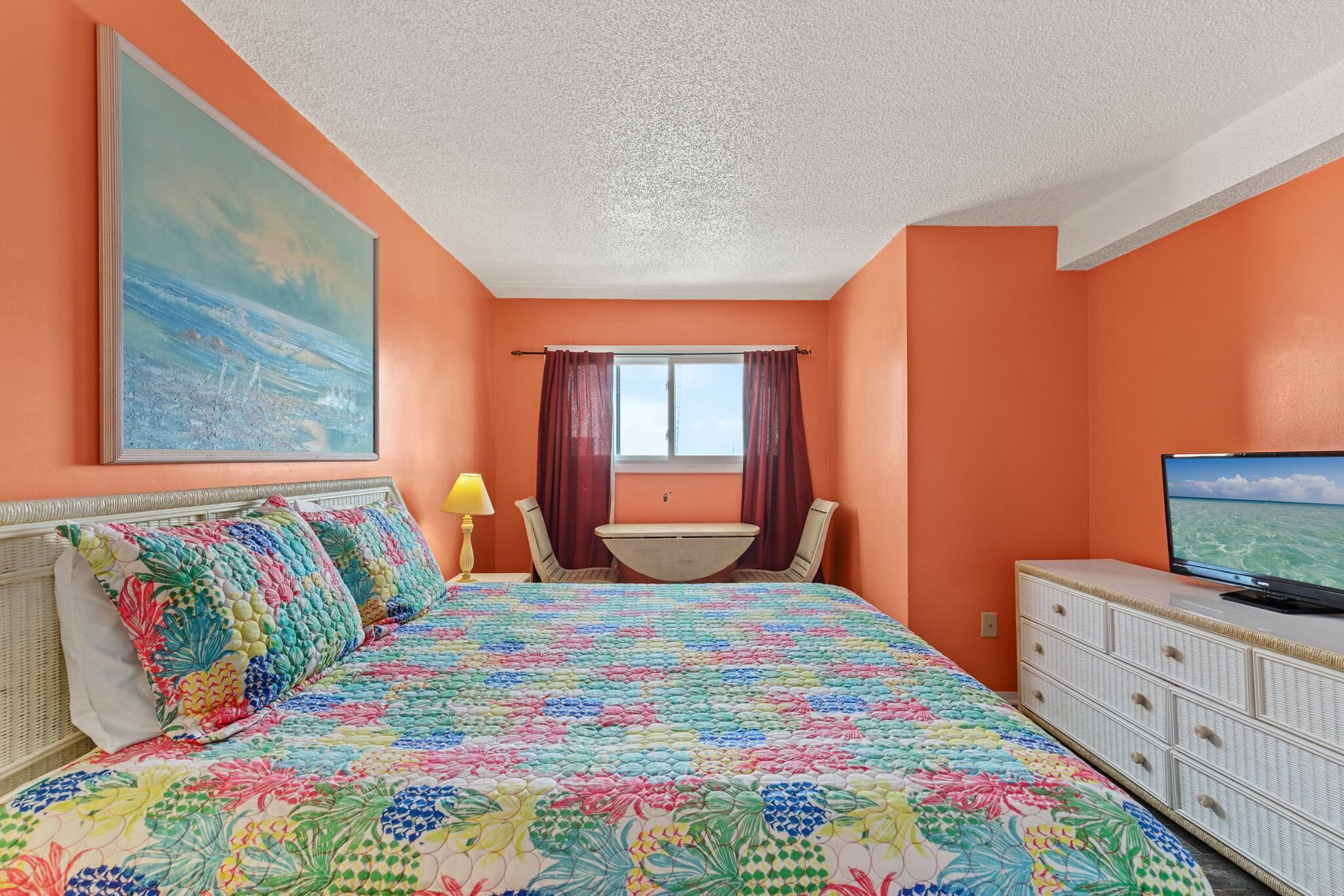 A bedroom with a bed, a television, a desk, and a window with curtains.