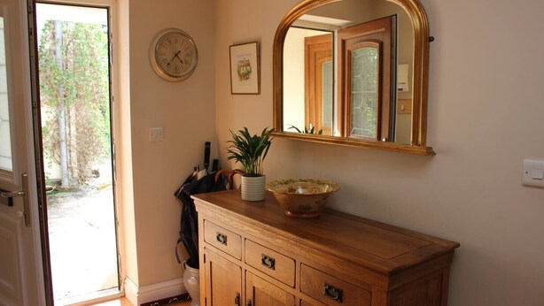 A wooden vanity with a mirror, a clock, and a framed picture on the wall. - Quaint 1-bedroom house in Cheltenham (Cheltenham)