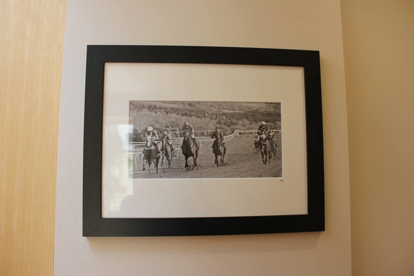 A framed black and white photograph of jockeys on horses in a race.