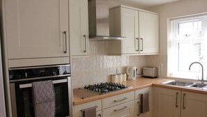 A modern kitchen with a gas stove, oven, and a window providing natural light. - Quaint 1-bedroom house in Cheltenham (Cheltenham)