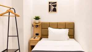 A hotel room with a bed, a nightstand, a wooden hanger, a small plant, and a wall art piece. - Hotel Poblado Boutique (Medellín)