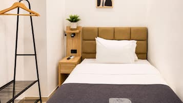 Une chambre d’hôtel comprenant un lit, une table de chevet, un cintre en bois, une petite plante et une œuvre d’art murale.