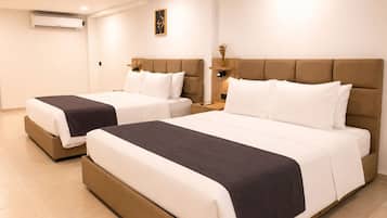 Habitación de hotel con dos camas, una mesita de noche, un aire acondicionado instalado en la pared y un objeto decorativo pequeño en la pared.