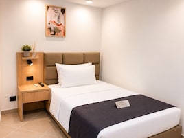 Quarto de hotel bem arrumado, com uma cama, mesa de cabeceira, abajur e uma pequena prateleira com uma planta.