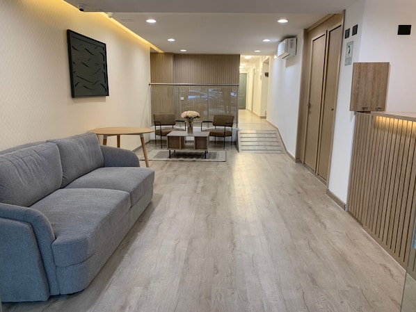 Ein modernes Wohnzimmer mit einem grauen Sofa, einem Esstisch mit Stühlen und einer Küchenzeile mit Holzschränken.
