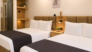 Habitación de hotel con dos camas, cabecero de madera, mesitas de noche con lámparas, una obra de arte colgada en la pared y una puerta que da a otra habitación.