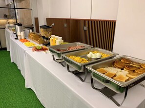 Una mesa de buffet con diversos alimentos, como hot dogs, huevos y tostadas.