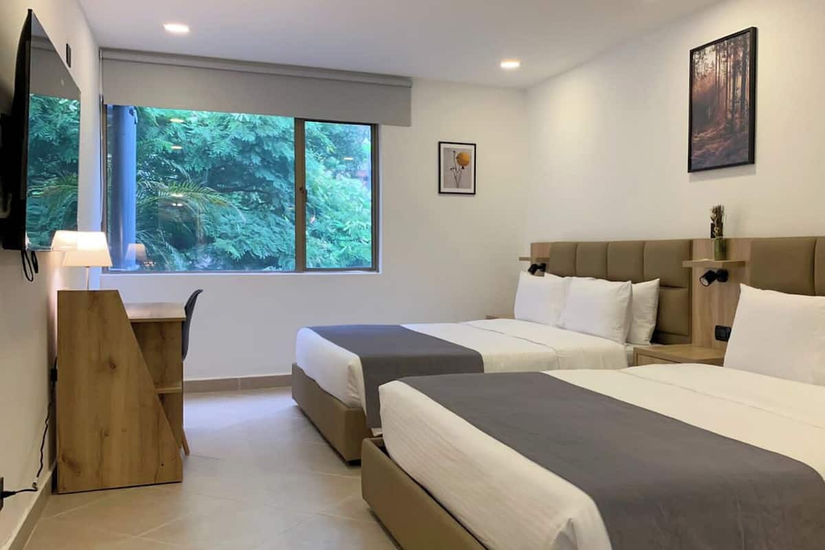 Een hotelkamer met twee bedden, een bureau en een groot raam met uitzicht op groen.