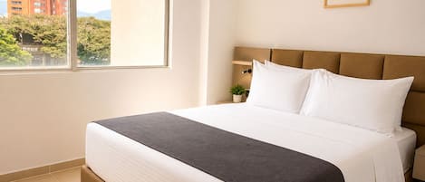 A hotel room with a bed, a window, a nightstand, and a framed picture on the wall.