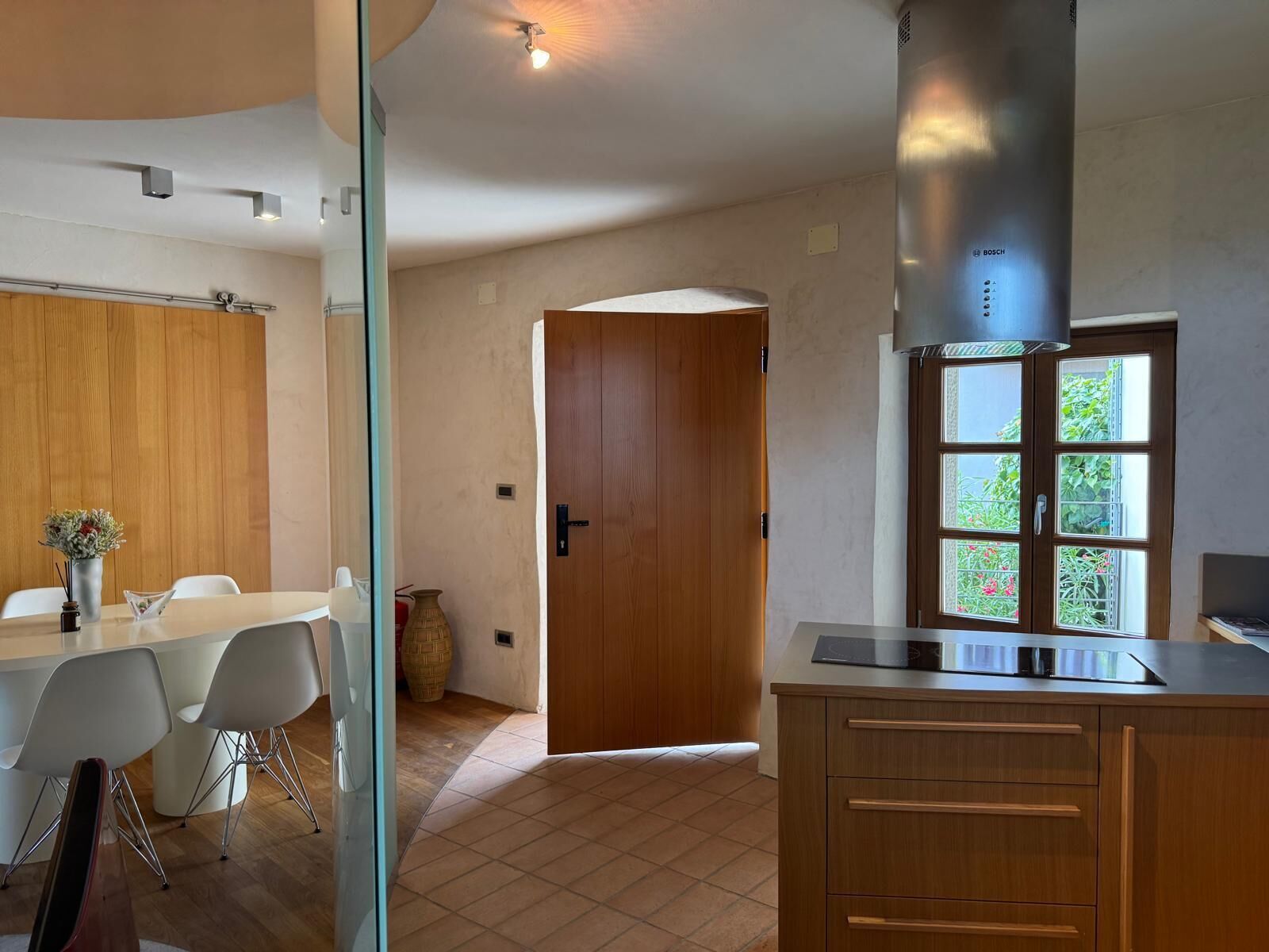A modern kitchen with wooden cabinets, a stainless steel range hood, and a window with a view of greenery.