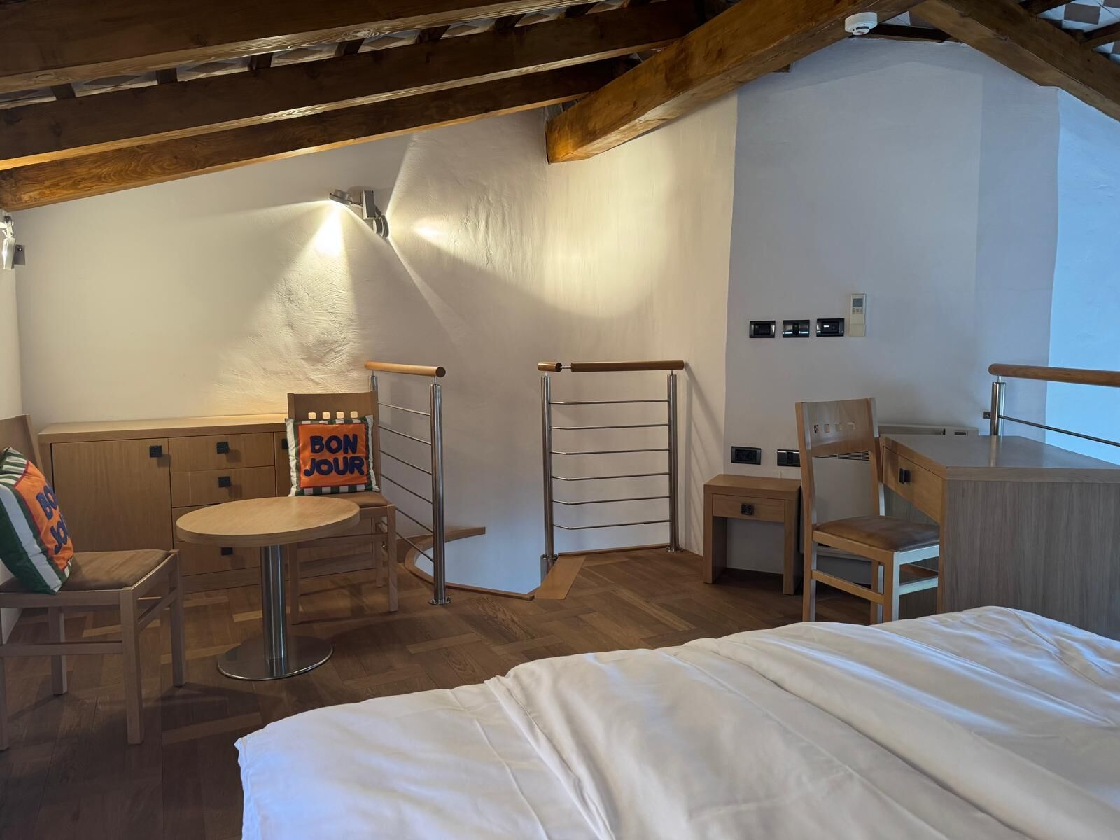 A cozy room with a bed, a small table, a chair, a desk, and a ladder.