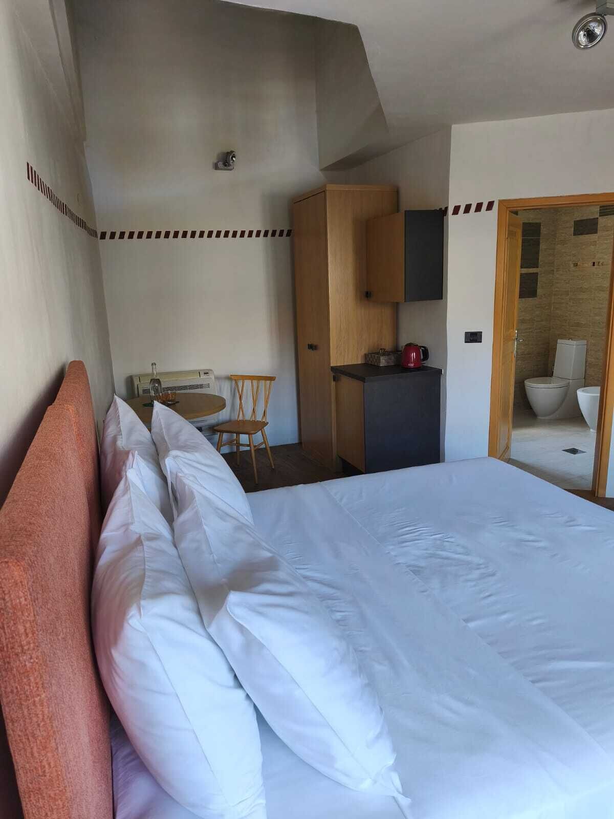 A hotel room with a large bed, a small dining table, a wooden cabinet, and a kitchenette.