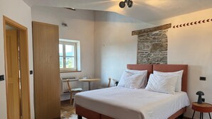 Un dormitorio con una cama grande, una pared de acento de piedra, piso de madera y una pequeña mesa con sillas.