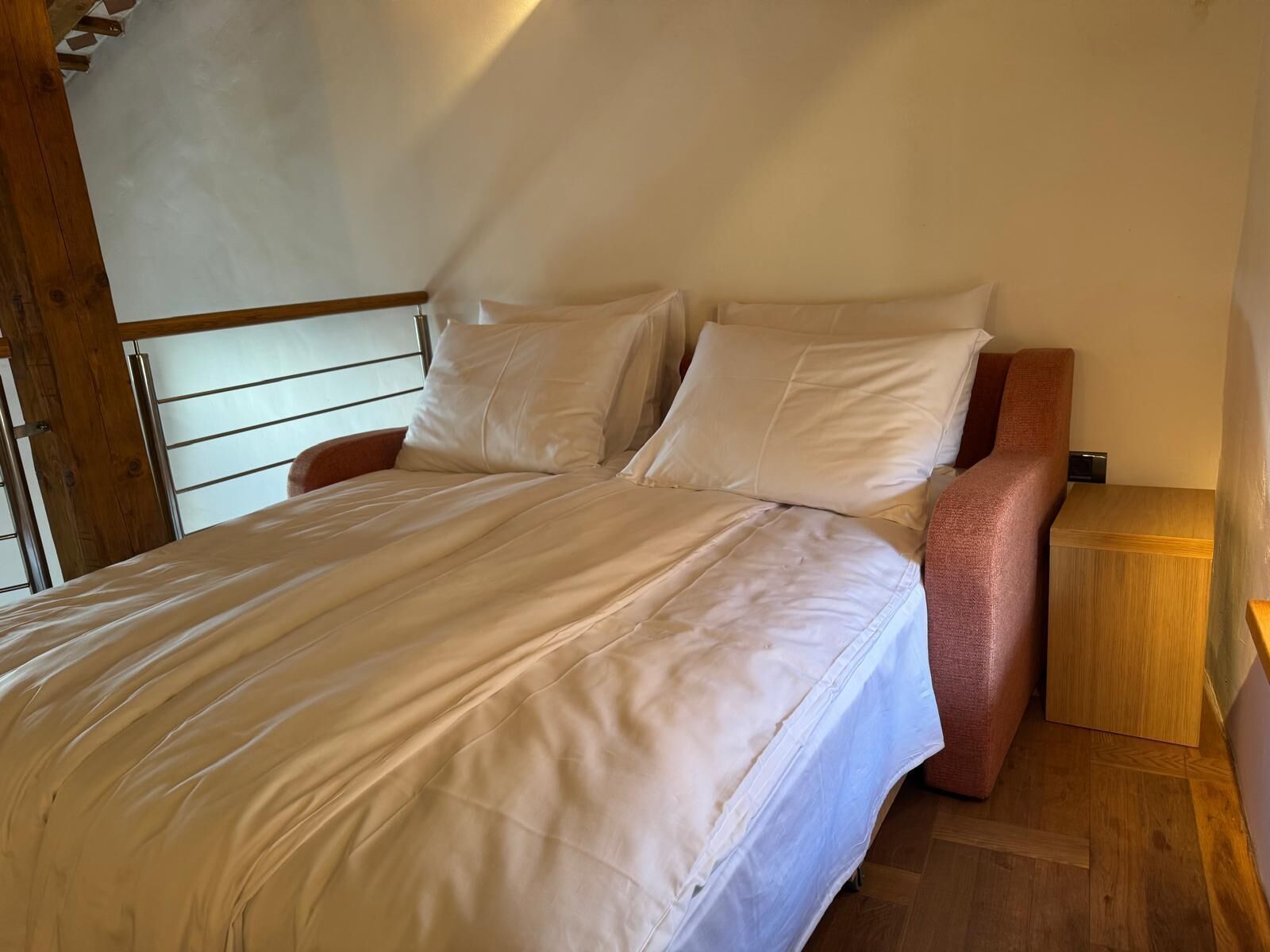 A bedroom with a bed, pillows, a wooden headboard, a nightstand, and a wooden floor.