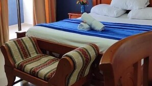 A bedroom with a bed, a chair, a nightstand, and a painting on the wall. - Hotel Dorado Baq (Barranquilla)