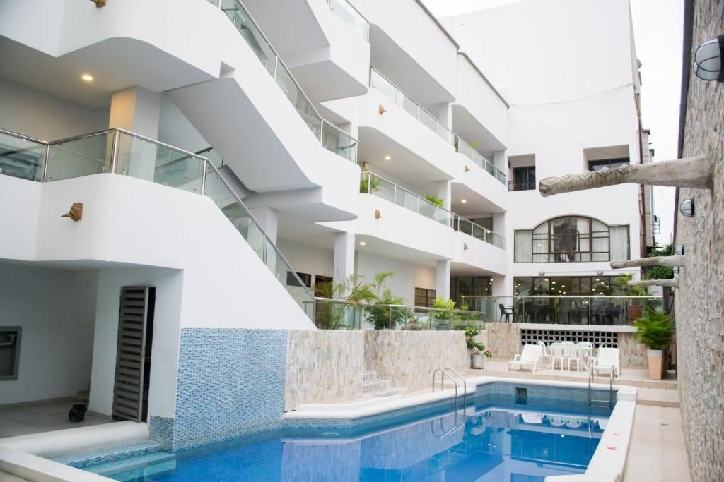 Un interior de hotel moderno con una piscina central, varios balcones y un comedor con mesas al aire libre.
