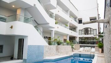 Un interior de hotel moderno con una piscina central, varios balcones y un comedor con mesas al aire libre.