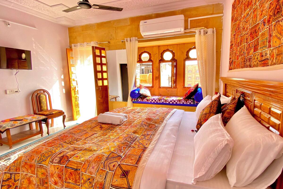A hotel room with a large bed, a wooden headboard, a television mounted on the wall, and an air conditioning unit.