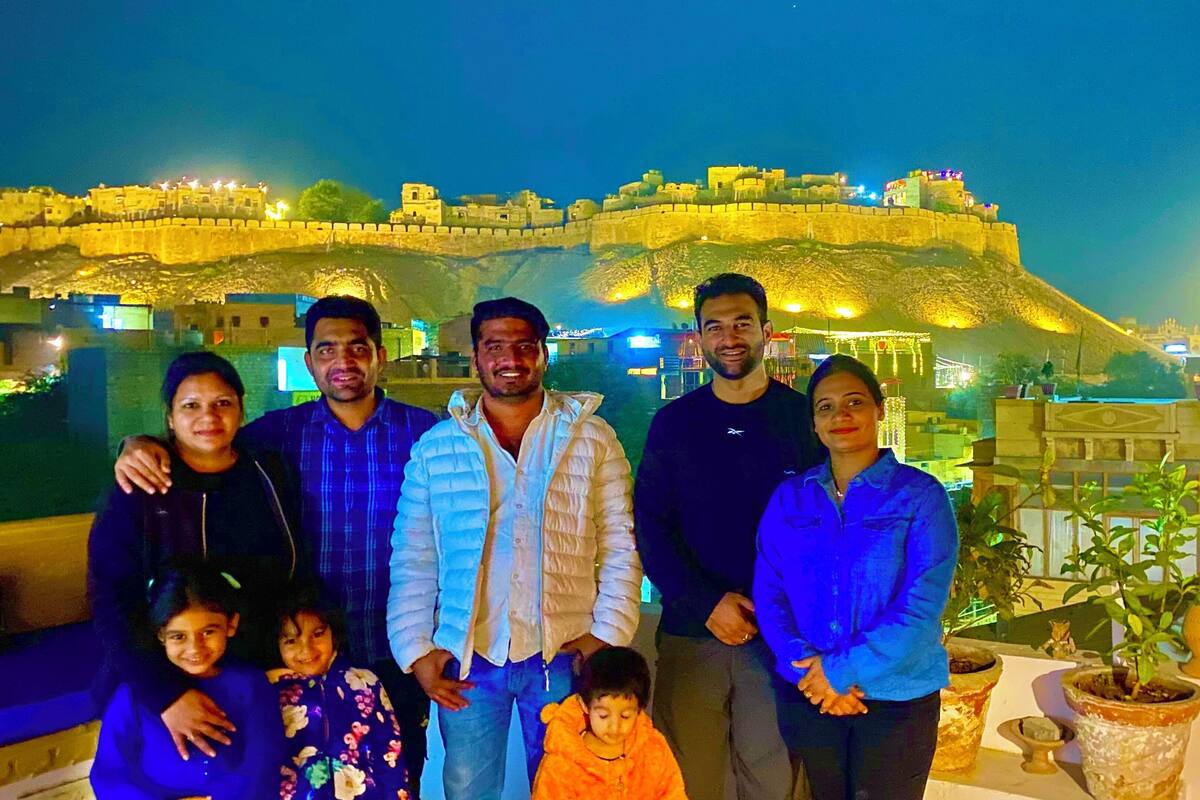 A group of people standing in front of a historic fort with a moat, under nighttime lighting.