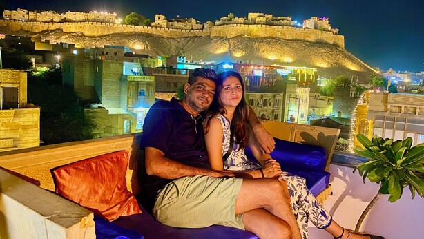 Un couple est assis sur un canapé bleu, avec en arrière-plan la vue d’un fort historique.