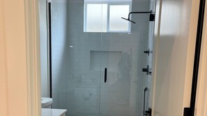 A narrow bathroom with a toilet, a vanity with drawers, a shower area, and a window above the shower. - Charming 2-bedroom guesthouse in peaceful Gladstone with WiFi, AC (Gladstone)