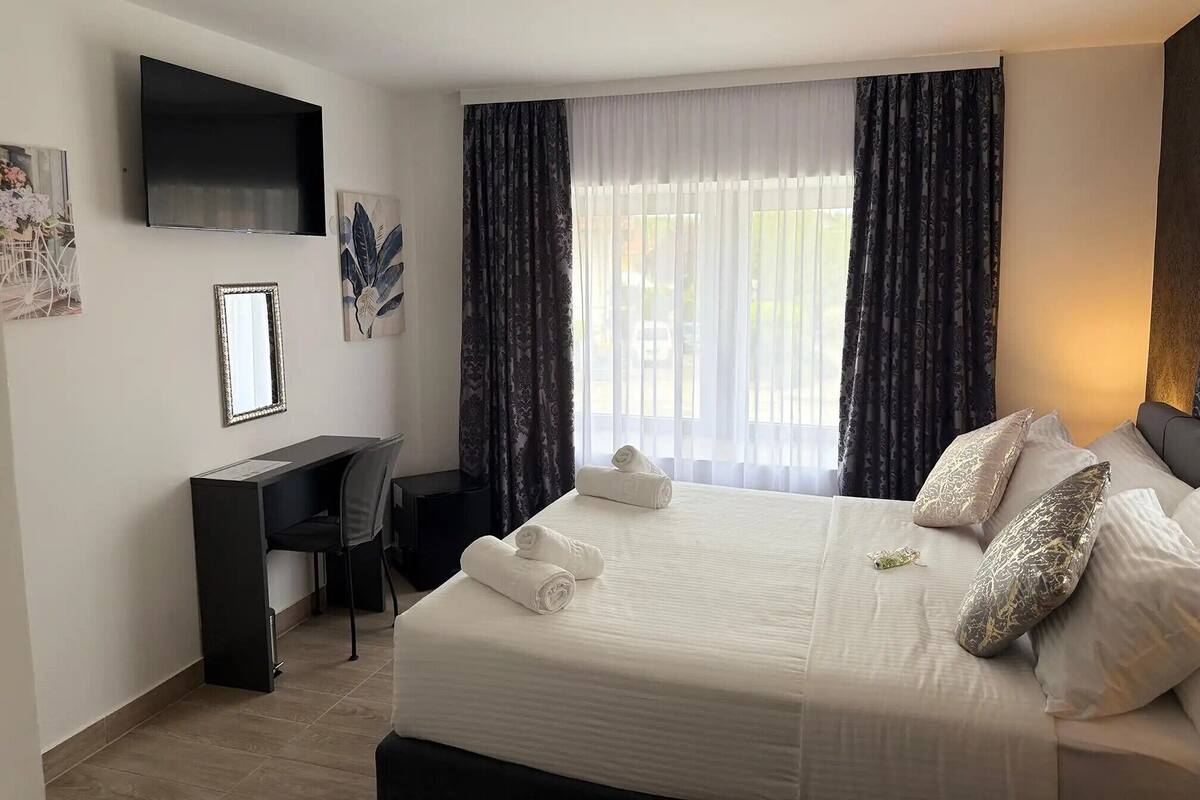 A hotel room with a bed, a desk, a chair, a TV, and a window with curtains.
