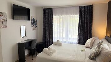 Habitación de hotel con cama, escritorio, silla, televisor y ventana con cortinas.