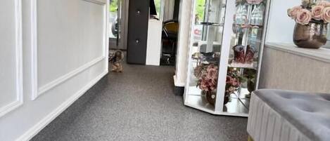 Un pasillo con alfombra gris, pared blanca con paneles, mueble de espejo con puertas de vidrio y un banco gris con patas doradas.