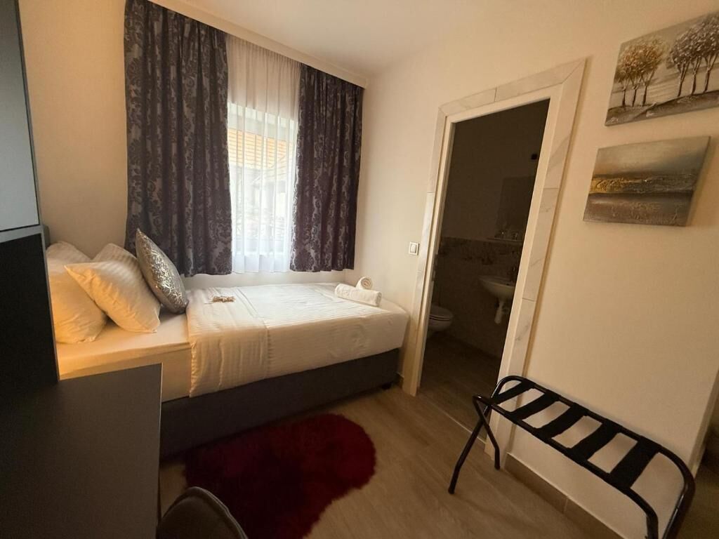 Un dormitorio con cama, escritorio, silla, un tapete rojo y un baño visible a través de una puerta abierta.