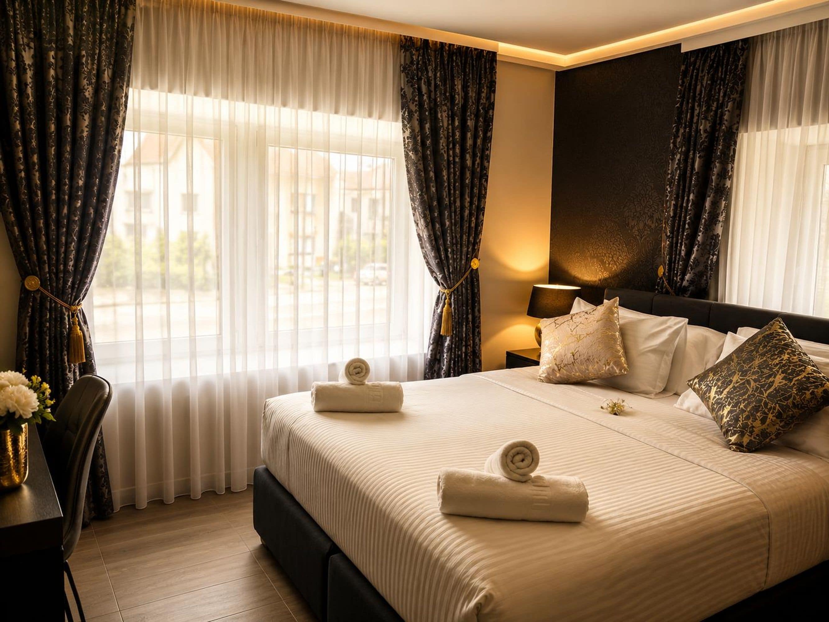 A hotel room with a bed, curtains, a bedside table with a lamp, and a view through the window.