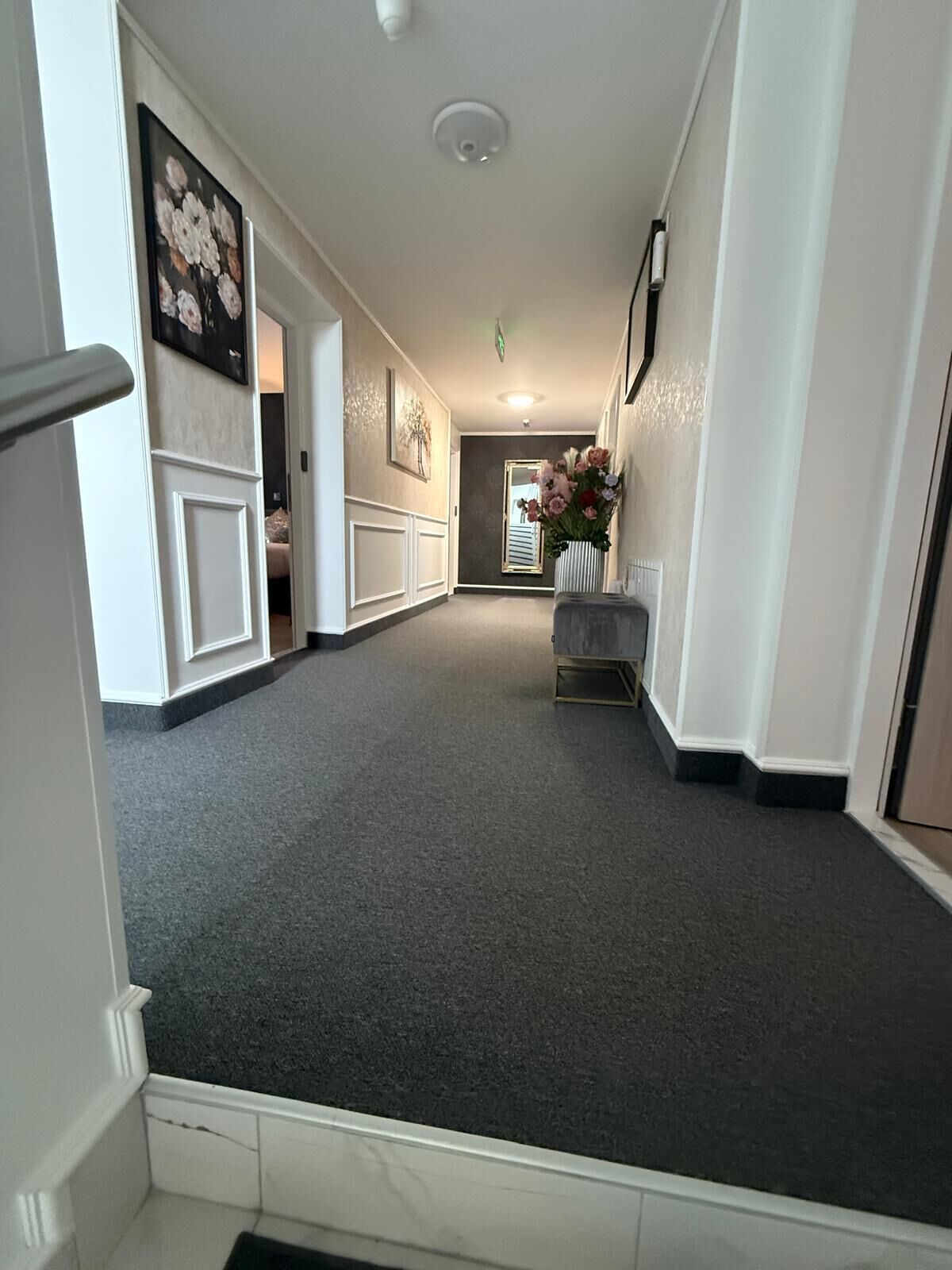 A hallway with a grey carpet, white walls, and a white door at the end.