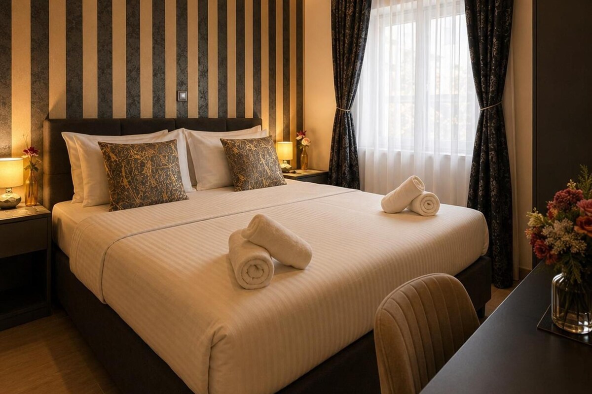 A hotel room with a large bed, two bedside tables, a desk, and a window with curtains.