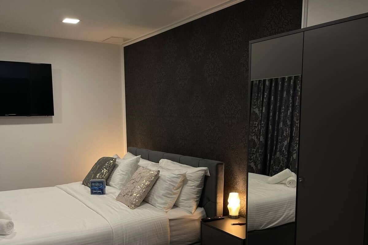 A modern hotel room with a bed, bedside table, mirror, and wardrobe.