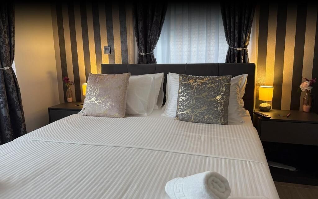 A neatly made bed with white bedding, two decorative pillows, and a rolled towel on the bed.