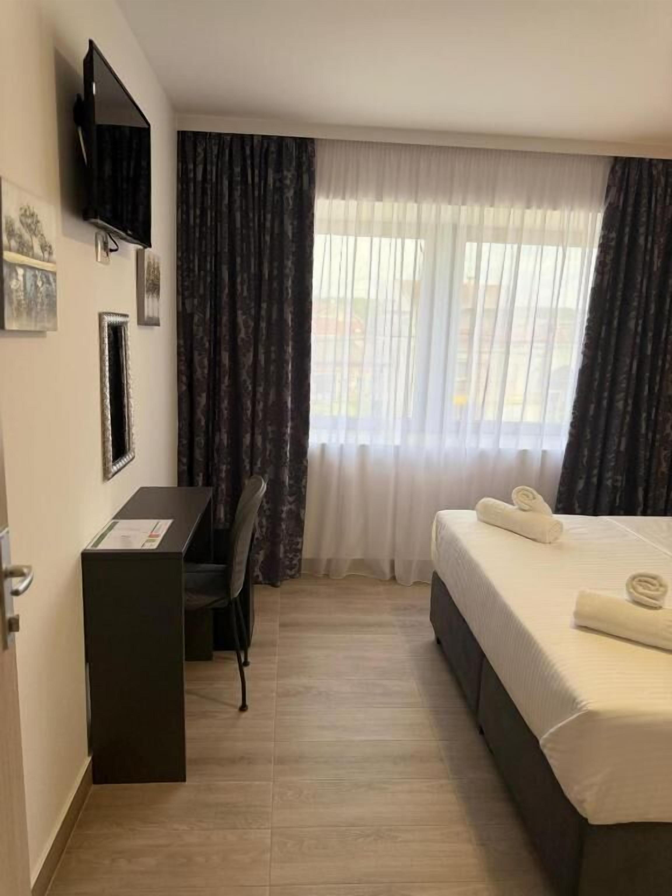 A hotel room with a bed, a desk, a chair, a television, and a window with curtains.
