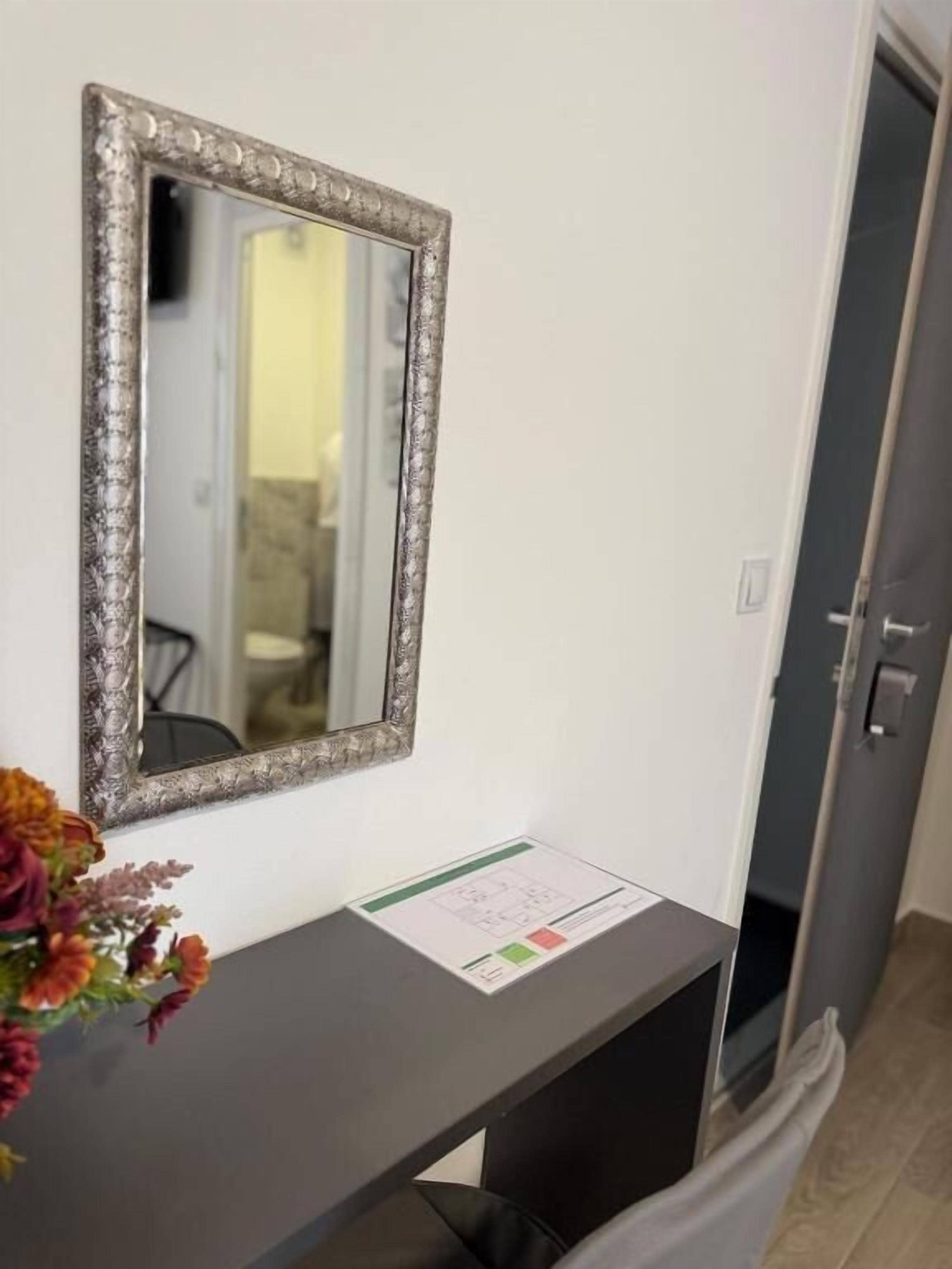 A room with a mirror on the wall, a small table with a vase of flowers, and a door leading to another room.