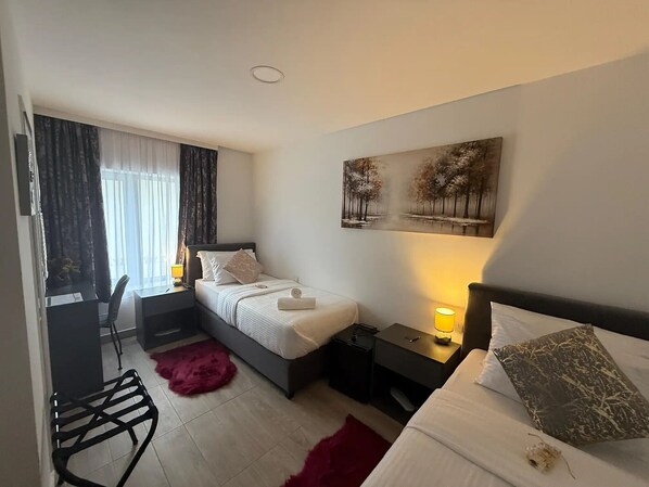 A hotel room with a bed, a desk, a chair, a red rug, and a painting on the wall.