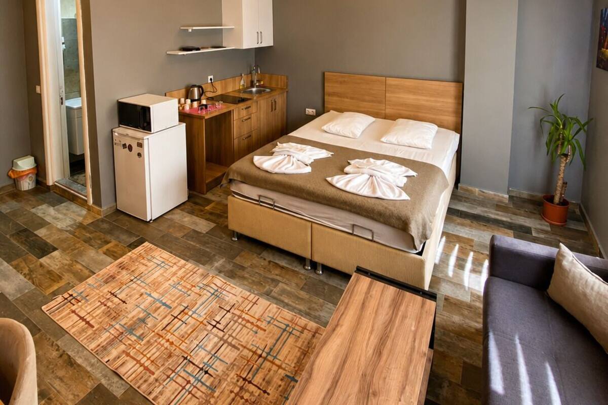 A compact hotel room with a bed, a small kitchenette, a seating area, and a bathroom.