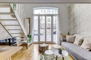 Un salon moderne avec un escalier, un canapé, une table basse et une vue sur la rue, visible à travers une porte vitrée.