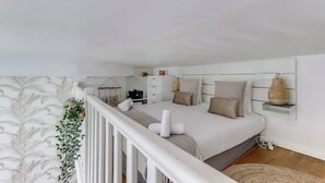 Une chambre avec un grand lit, des murs blancs, une balustrade blanche et une vue sur le balcon.