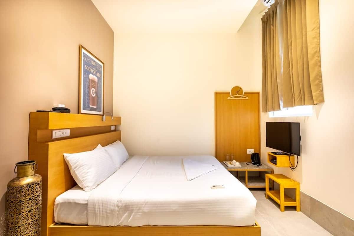 Una habitación de hotel con cama, mesita de noche, televisión y ventana con cortinas.