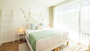 Un dormitorio con cama, mesitas de noche, una escalera y una ventana con cortinas.