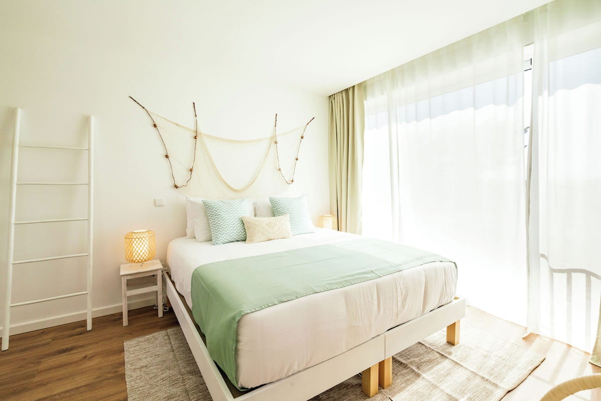 Une chambre à coucher avec un lit, des tables de chevet, une échelle et une fenêtre avec des rideaux.