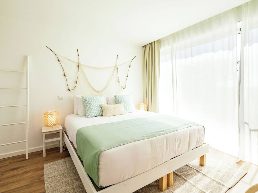 A bedroom with a bed, bedside tables, a ladder, and a window with curtains.